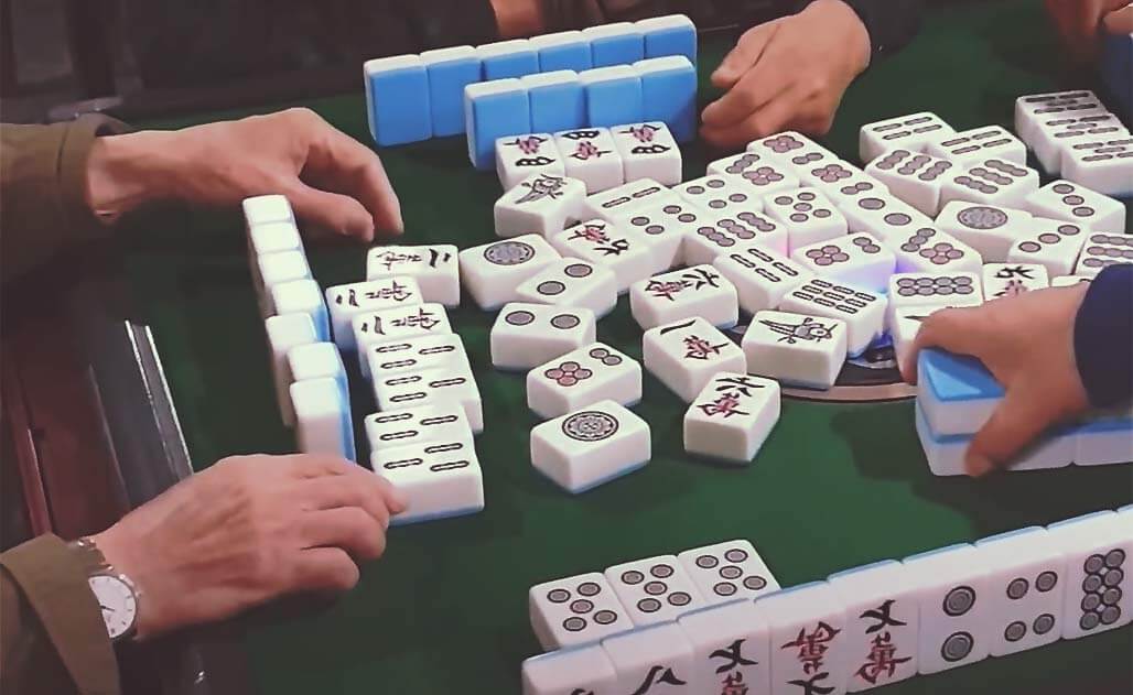 Een groep Chinezen die een spel mahjong spelen, met traditionele stenen op een groene speeltafel